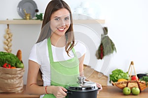 Young happy woman cooking soup in the kitchen. Healthy meal, lifestyle and culinary concept. Smiling student girl