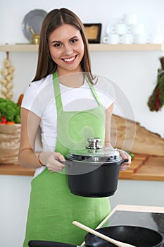 Young happy woman cooking soup in the kitchen. Healthy meal, lifestyle and culinary concept. Smiling student girl