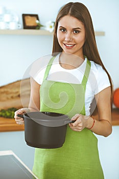 Young happy woman cooking soup in the kitchen. Healthy meal, lifestyle and culinary concept. Smiling student girl