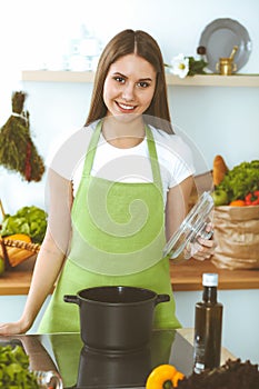 Young happy woman cooking soup in the kitchen. Healthy meal, lifestyle and culinary concept. Smiling student girl