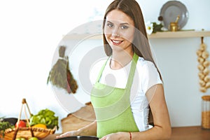 Young happy woman cooking soup in the kitchen. Healthy meal, lifestyle and culinary concept. Smiling student girl