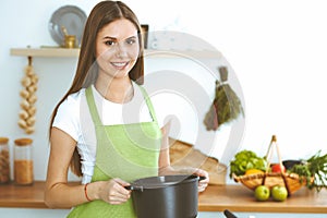 Young happy woman cooking soup in the kitchen. Healthy meal, lifestyle and culinary concept. Smiling student girl