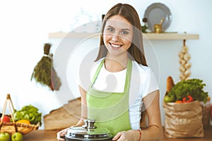 Young happy woman cooking soup in the kitchen. Healthy meal, lifestyle and culinary concept. Smiling student girl