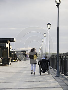 Young happy woman with disabled man in a wheelchair walking together on the quay - rear view