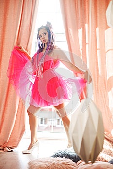 young woman with dreadlocks hairstyle wearing pink dress, doll style, bright make, up in the pink room.