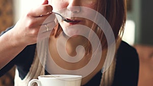 Young happy woman drinks coffee, stirring with a spoon milk foam