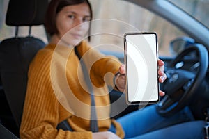 A young happy woman driving a car, she shows empty phone screen
