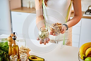 Young happy woman eating different nuts cashew, hazelnut, almond in modern kitchen. Healthy food and Dieting concept. Loosing