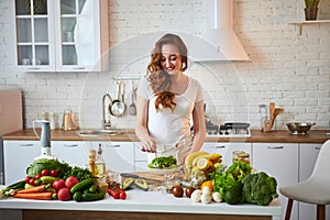 Young happy woman eating salad in the beautiful kitchen with green fresh ingredients indoors. Healthy food concept