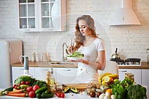 Young happy woman eating salad in the beautiful kitchen with green fresh ingredients indoors. Healthy food concept