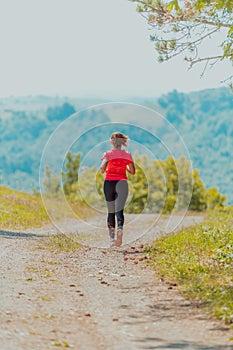 Young happy woman enjoying in a healthy lifestyle while jogging on a country road through the beautiful sunny forest