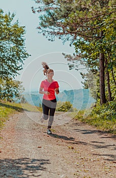 Young happy woman enjoying in a healthy lifestyle while jogging on a country road through the beautiful sunny forest