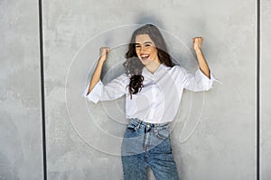 Young happy woman exults pumping fists ecstatic celebrates success isolated on gray wall background photo