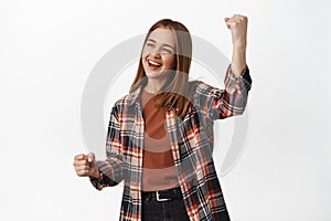 Young happy woman fist pump, laughing and smiling, cheering or rooting for team, looking aside at copy space