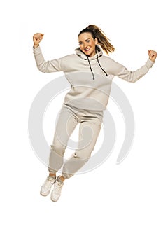 A young happy woman in a gray tracksuit jumping against a white background in the studio