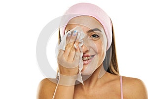 Young happy woman with headband cleans her face with wet wipes