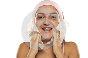 Young happy woman with headband cleans her face with wet wipes on white background