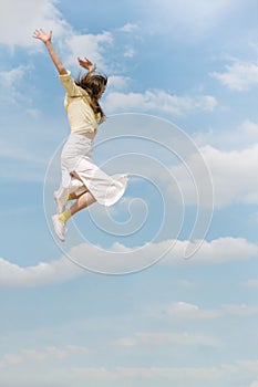 Young happy woman with her hands raised up during jump against the blue sky. Young girl flying high in blue sky