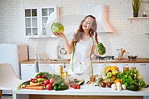 Young happy woman holding broccoli and cabbage in the beautiful kitchen with green fresh ingredients indoors. Healthy food and