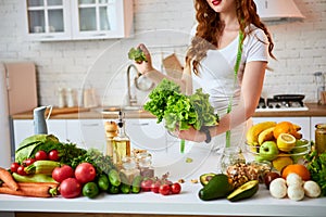 Young happy woman holding lettuce leaves for making salad in the beautiful kitchen with green fresh ingredients indoors. Healthy