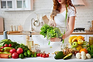 Young happy woman holding lettuce leaves for making salad in the beautiful kitchen with green fresh ingredients indoors. Healthy