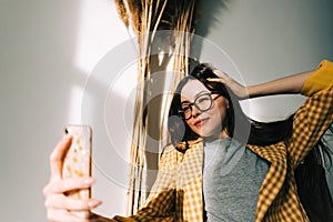 Young happy woman holding smartphone looking on cell using mobile phone technology at home, taking selfie for social media or