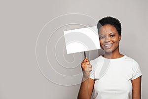Young happy woman holding white empty banner singboard in her hand on gray background