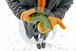 a young happy woman holds a cypress branch in yellow mittens in her hands. View from above