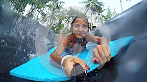 Young happy woman holds Go Pro action camera jumps in the pool in the attraction Slip N Fly on island Koh Phangan in