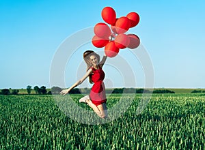 Young happy woman jumping with red balloons on green summer field