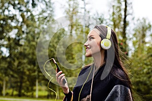 Young happy woman listening music from smartphone with headphones in a quiet Park