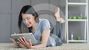 Young happy woman lying on the floor and using tablet computer at home