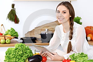 Young happy woman is making online shopping by tablet computer while smiling. Housewife looking for a new recipe fo