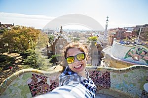 Young happy woman making selfie portrait with smartphone in Park Guell, Barcelona, Spain. Beautiful girl looking at