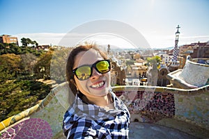 Young happy woman making selfie portrait with smartphone in Park Guell, Barcelona, Spain. Beautiful girl looking at
