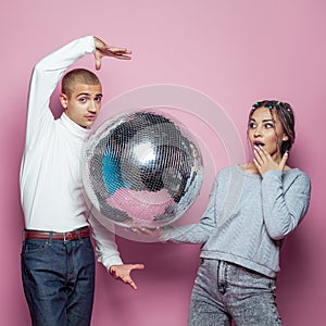 Young happy woman and man with disco ball posing on pink background
