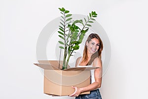 The young happy woman is moving into a new house. She brings a box with her favorite plant to her new home