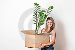 The young happy woman is moving into a new house. She brings a box with her favorite plant to her new home