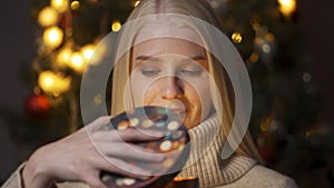 Young happy woman opening present box close-up. Beautiful model holding christmas gift, lying on sofa in decorated