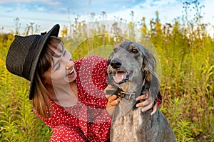 Young happy woman plays with her purebred gray dog in the park