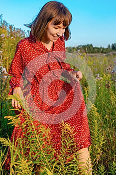 A young happy woman in a red dress walks in the field on a warm sunny day