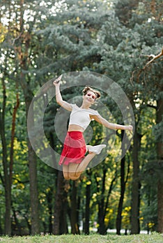 A young happy woman in a red skirt jumps high in a summer park, having fun