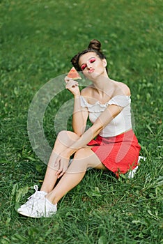 A young happy woman in a red skirt and a white T-shirt blows a kiss while holding a watermelon in her hand