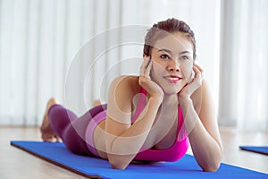 Young happy woman relaxing on yoga mat in gym