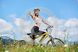 Young happy woman riding bicycle in the mountains at summer day