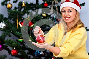 Young happy woman in santa hat is holding a christmas ball