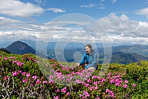 Young happy woman sitting among blooming wild rhododendron. Rhododendron flowers blossom on the Ukraine peak Pip Ivan