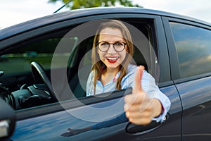 Young happy woman sitting in a car with thumb up