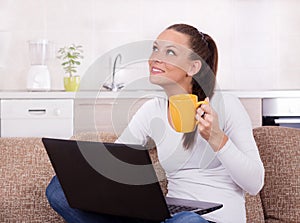 Woman with laptop and cup of coffee on sofa