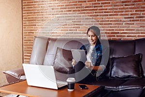 Young happy woman sitting on sofa and using a tablet, laptop on the table in front of her. relaxing concept